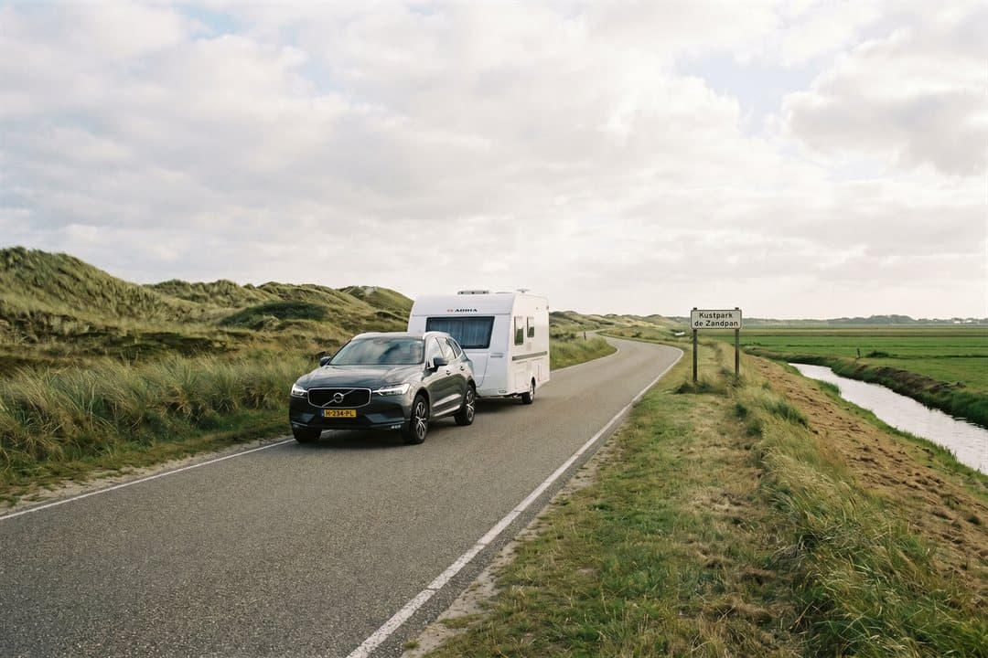 Auto met toercaravan op een Nederlandse kustweg langs de duinen