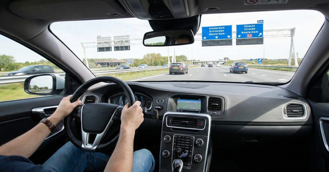 Zicht vanuit een auto op de snelweg met blauwe wegwijzers boven de weg